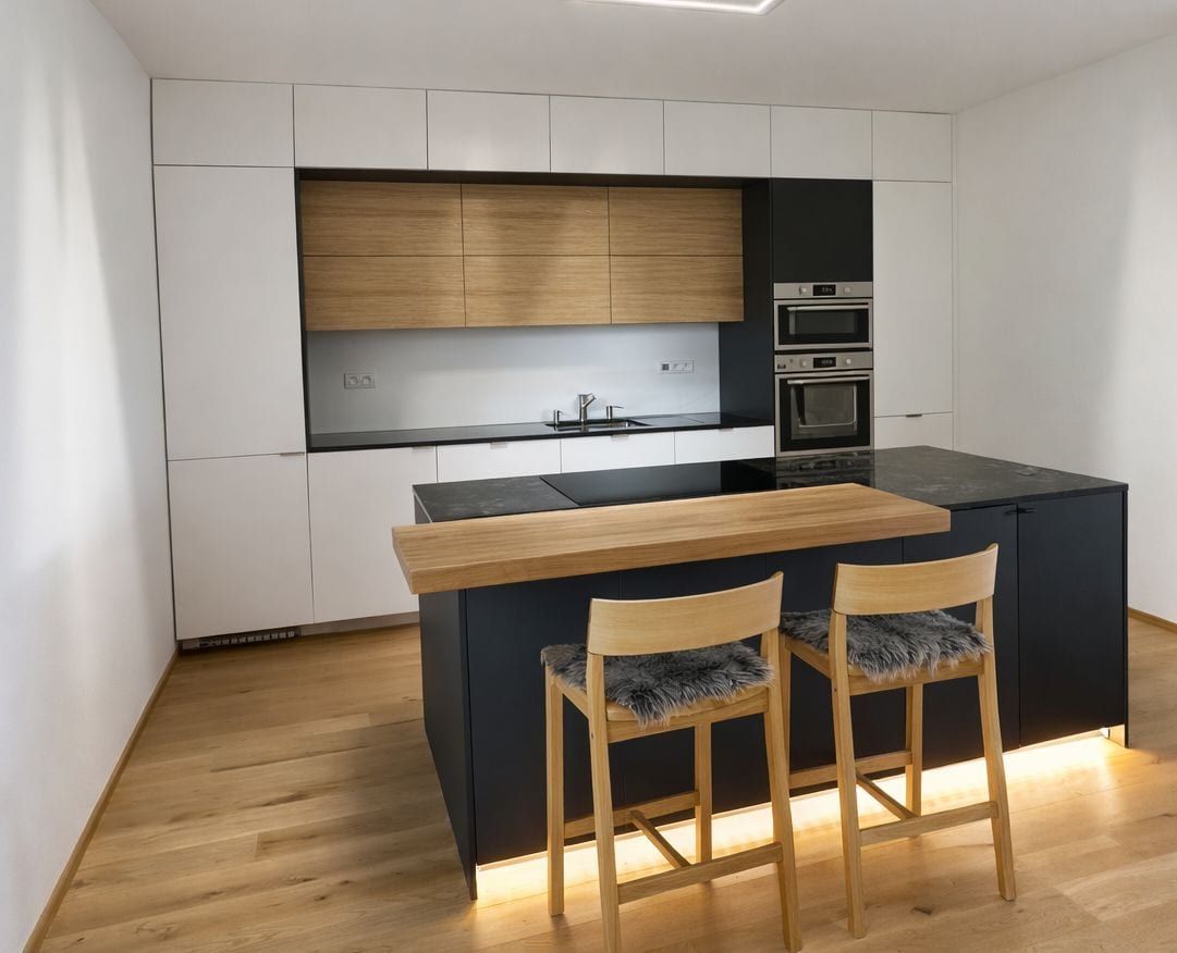 Kuchyně s tmavým ostrůvkem a barovými židlemi, bílé fronty a dubová dýha nad varnou deskou